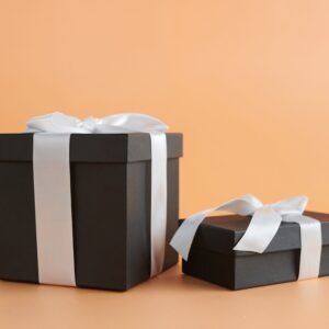 Two black gift boxes with white ribbons on a beige background, perfect for celebrations.
